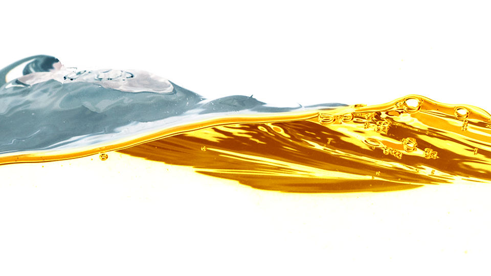 Abstract image of a wave of golden liquid meeting a softer grey wave against a white background