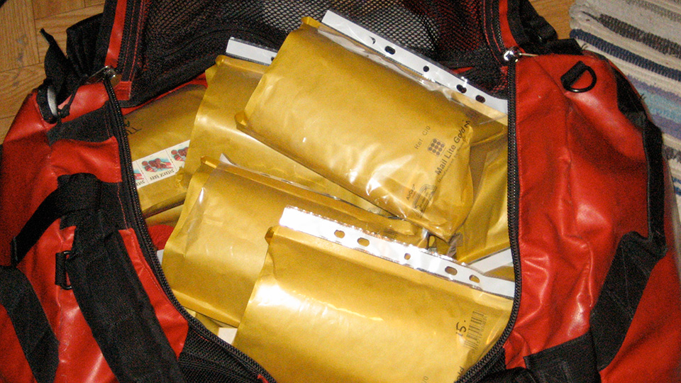 Open red and black duffel bag packed with several gold padded envelopes ready for distribution