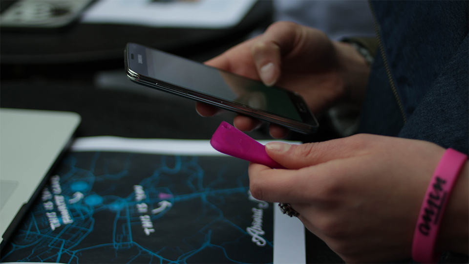 Close-up of hands holding a smartphone and a pink NFC-tagged card over a printed map