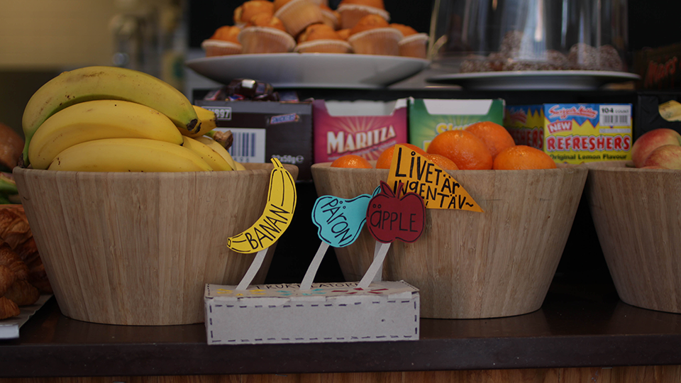 Breakfast buffet bowls of fruit and snacks with a small cardstock sign holding paper banana and label cutouts