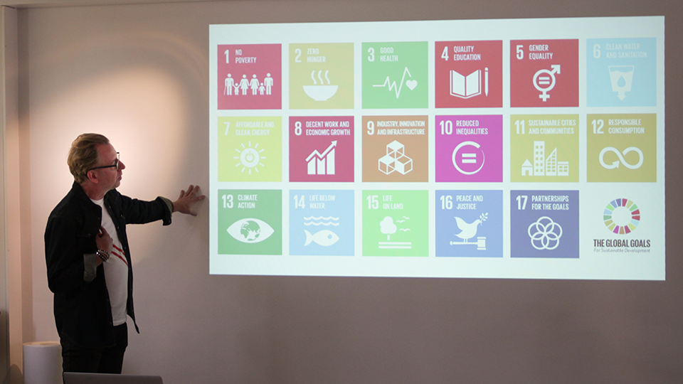 Presenter standing beside a projected grid of the UN Sustainable Development Goal icons during a talk