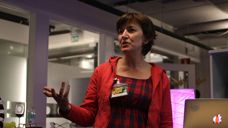 Kia Höök speaking and gesturing while wearing an IoT name badge over a red checked shirt, in a meetup space