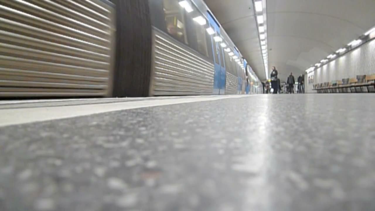 Video still: low-angle view along a Stockholm metro platform as a train passes, the speckled floor filling the foreground